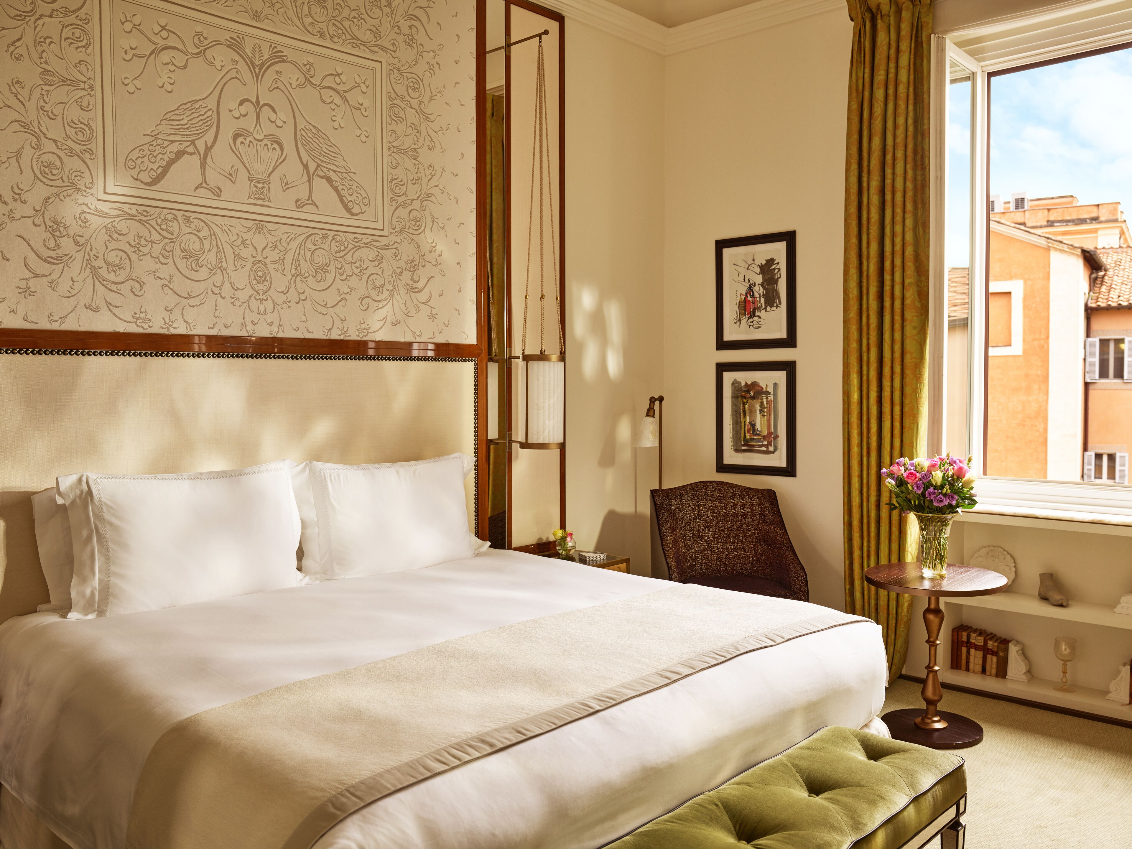 A neatly made bed with white linens, a green upholstered bench, and a vase of flowers on a small table.