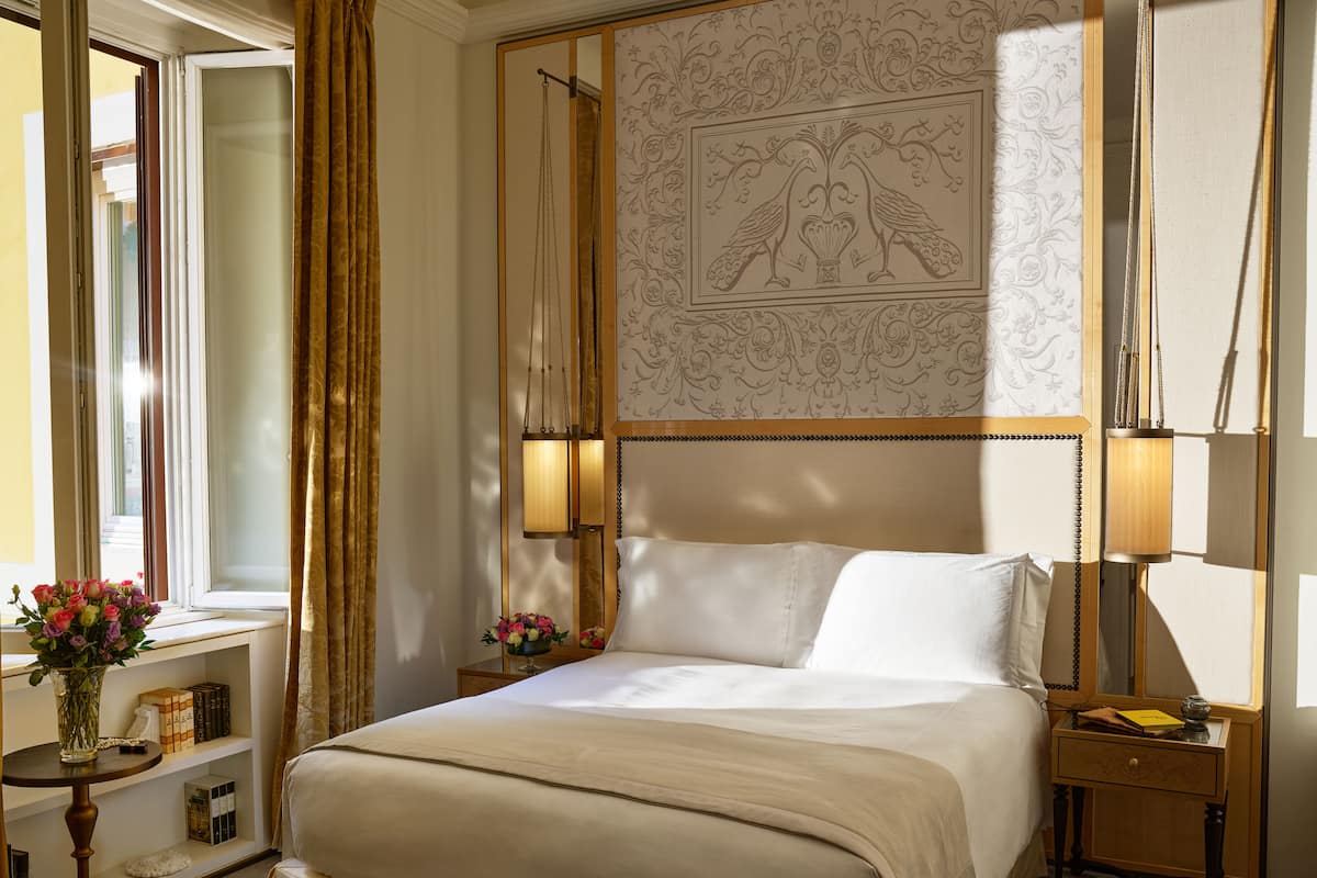 Habitación de hotel con una cama grande, dos mesitas de noche, una lámpara de noche, una ventana con cortinas y un panel decorativo en la pared.