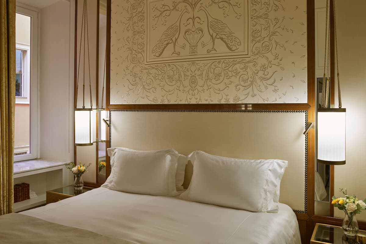Habitación de hotel con una cama grande, un panel decorativo en la pared, una mesita de noche con lámpara y una ventana con cortinas.