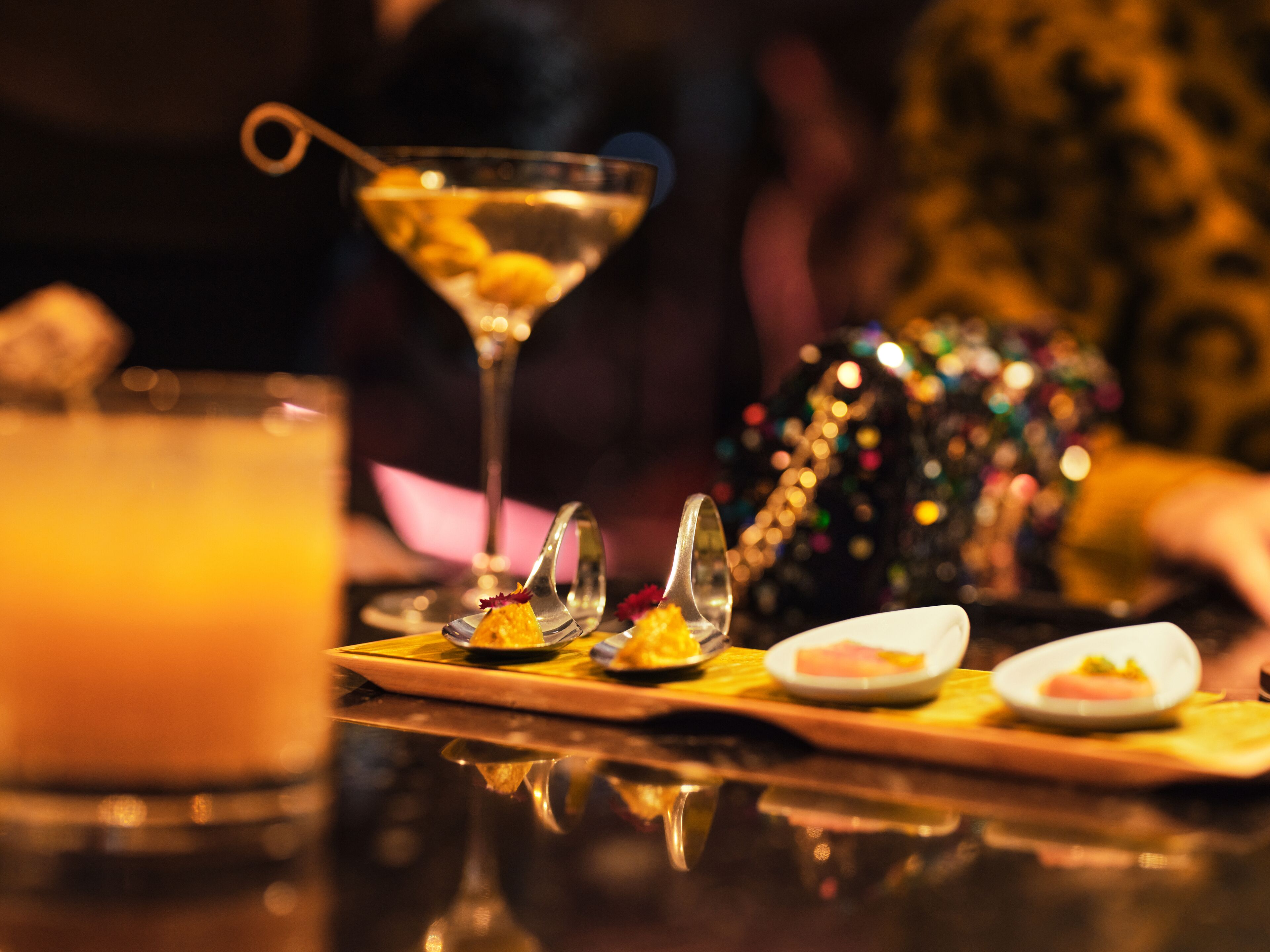 A bar setting with a martini glass, a cocktail, and a plate with food items.