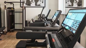 Een sportschool met trainingsapparatuur, een loopband en een scherm dat trainingsopties toont.