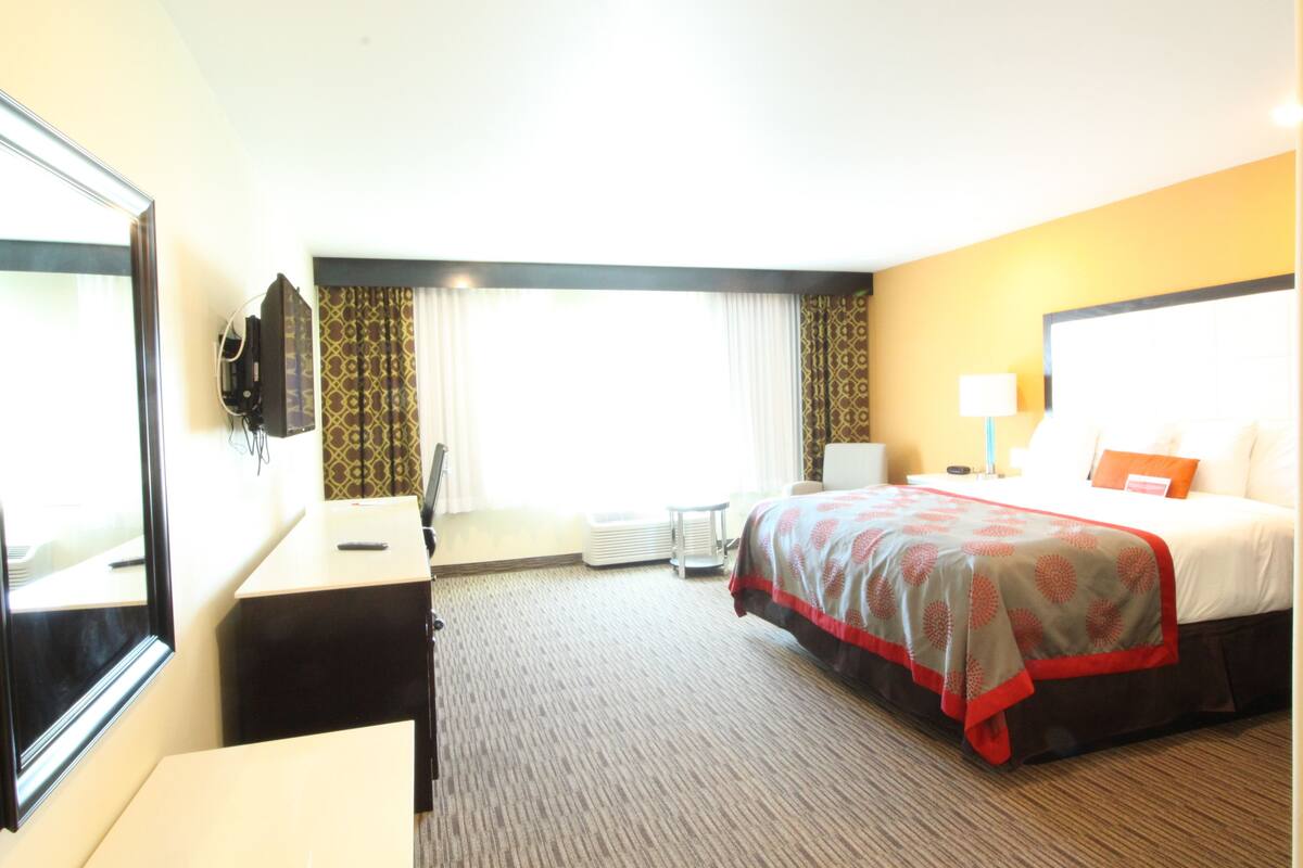 Ein Hotelzimmer mit Bett, Nachttisch, Schreibtisch, Stuhl und einem großen Spiegel.
