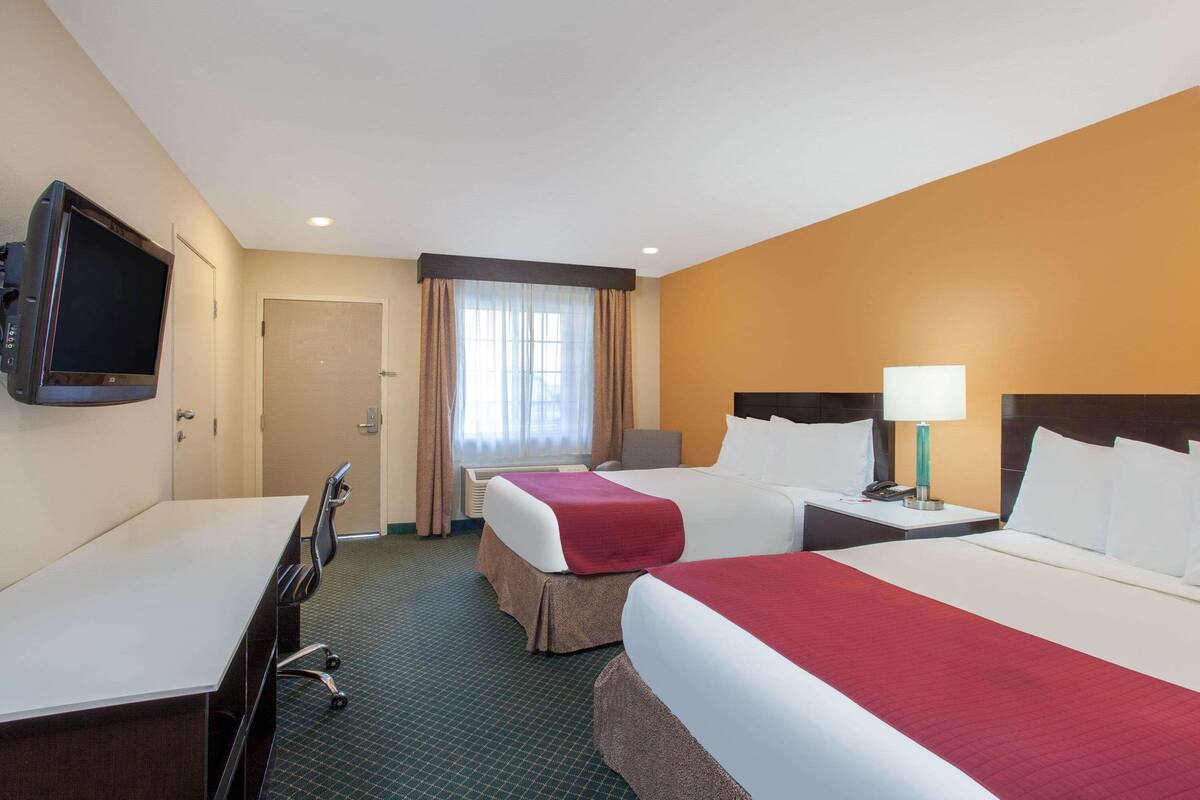 Ein Hotelzimmer mit zwei Betten, einem Schreibtisch, einem Fernseher und einem Fenster mit Vorhängen.
