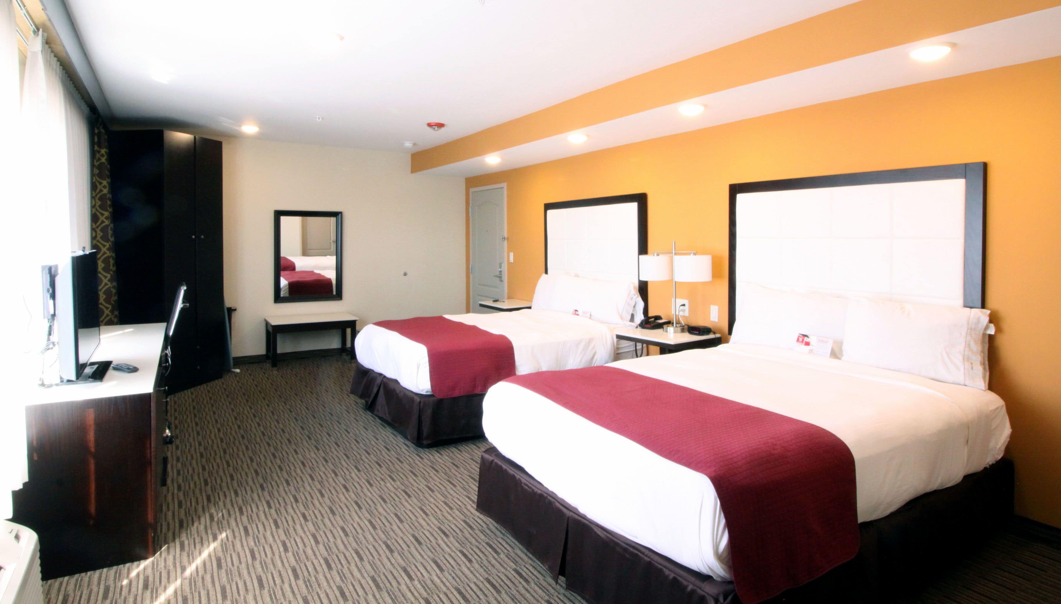 A hotel room with two beds, a desk, a chair, a mirror, and a lamp.