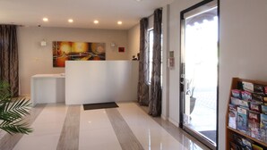 A reception area with a white reception desk, a large abstract painting on the wall, a potted plant, and a bookshelf with magazines. - Ramada by Wyndham Culver City (Culver City)