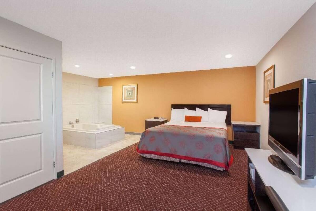 Ein Hotelzimmer mit Bett, Fernseher, Badezimmer mit Badewanne und einer weißen Tür.