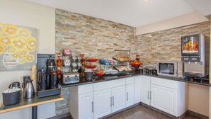 A kitchen with a stone backsplash, white cabinets, a coffee station, and a fruit and juice dispenser. - Ramada by Wyndham Culver City (Culver City)