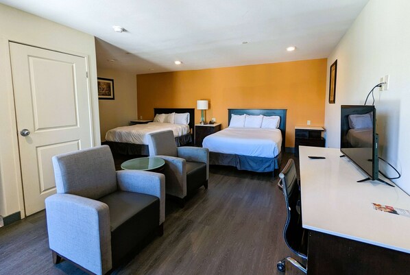Une chambre d’hôtel avec deux lits, un bureau, une chaise, une petite table et un téléviseur.