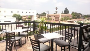 A balcony with a table and chairs, overlooking a street with parked cars and buildings. - Ramada by Wyndham Culver City (Culver City)