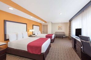 Two spacious beds with matching nightstands and lamps, a sofa, flat-screen TV, desk, and wardrobe.
