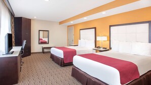 A hotel room with two beds, a desk, a chair, a mirror, and a nightstand with a lamp. - Ramada by Wyndham Culver City (Culver City)