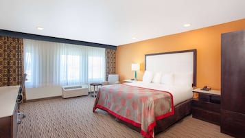A hotel room with a large bed, a desk, a chair, a lamp, and a wardrobe.