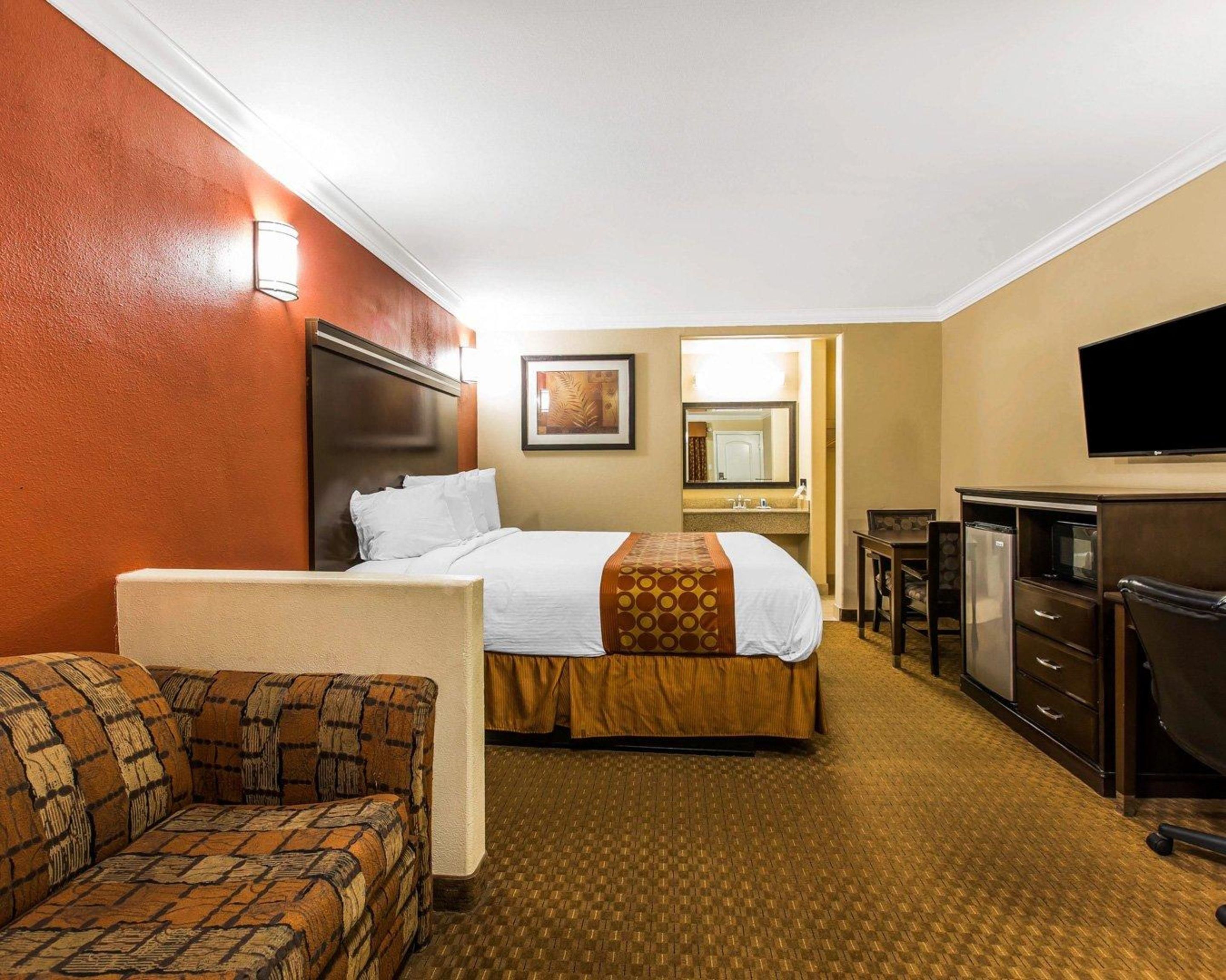 Hotelkamer met een bed, een bank, een bureau, een televisie en een badkamer die door een open deur zichtbaar is.