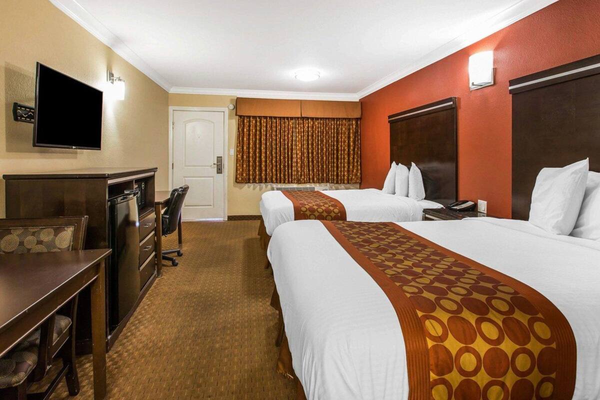 Ein Hotelzimmer mit zwei Betten, einem Schreibtisch mit Stuhl, einem Fernseher und einer Minibar.