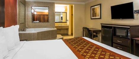 A hotel room with a large bed, a bathroom with a bathtub, a desk with a chair, a television, and a microwave.