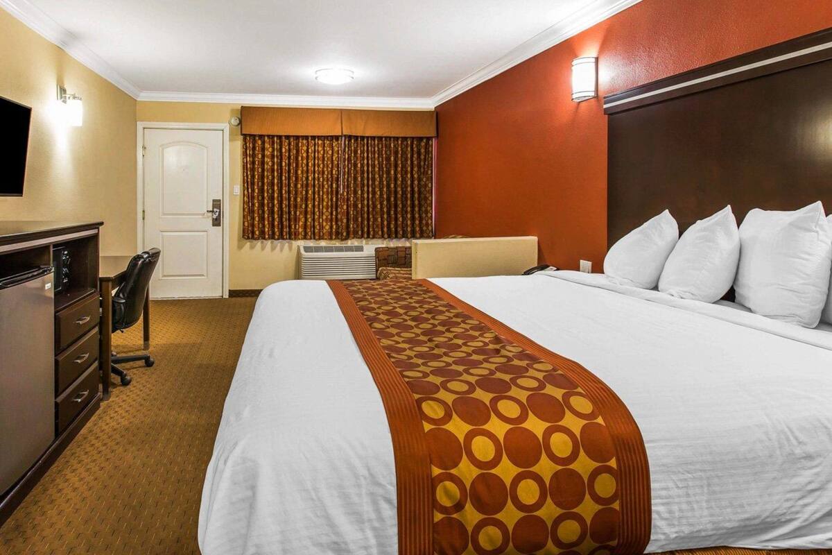 Ein Hotelzimmer mit einem großen Bett, einem Schreibtisch mit Stuhl, einem Fernseher und einem Fenster mit Vorhängen.