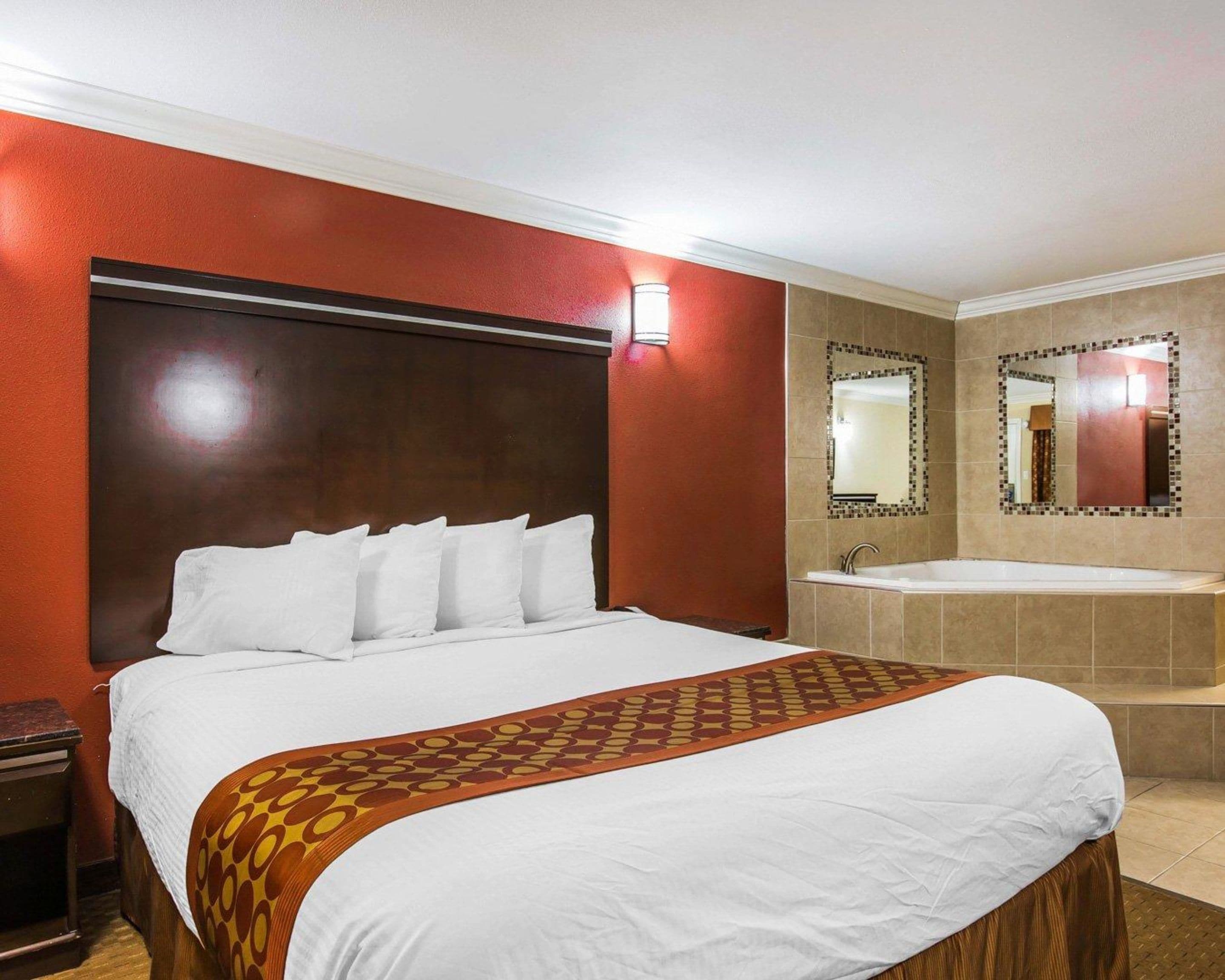 A hotel room with a large bed, a bathroom with a bathtub, and two mirrors on the wall.