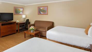 Habitación de hotel con dos camas, televisión, escritorio con lámpara, una silla y dos cuadros en la pared.