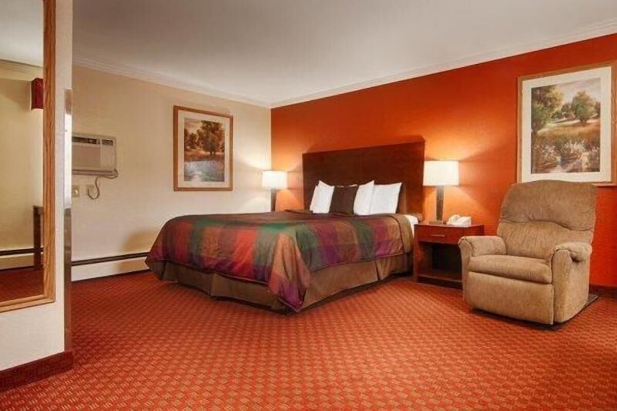 Una habitación de hotel con una cama, una silla, una mesita de noche y dos lámparas de pared.