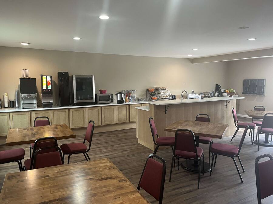 A modern kitchen area with built-in appliances, wooden tables, and red chairs.