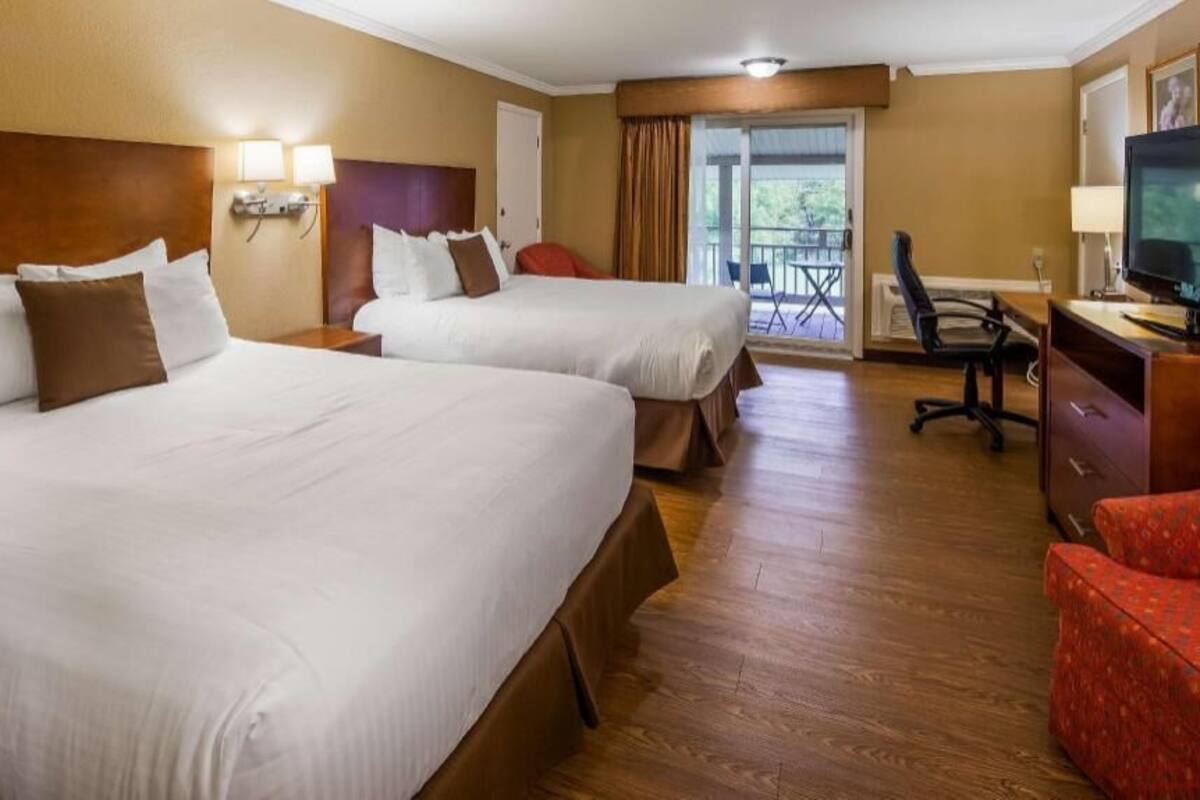 A hotel room with two beds, a desk with a TV, and a balcony.
