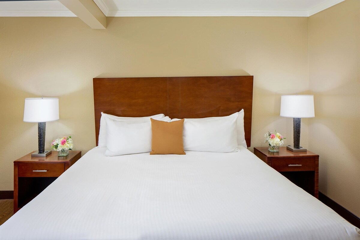 Una habitación de hotel con una cama grande, dos mesitas de noche con lámparas y un cabecero de madera.