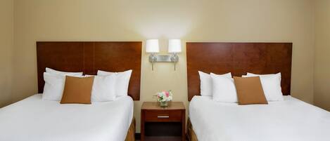 A hotel room with two beds, a nightstand with a lamp, and a vase with flowers.