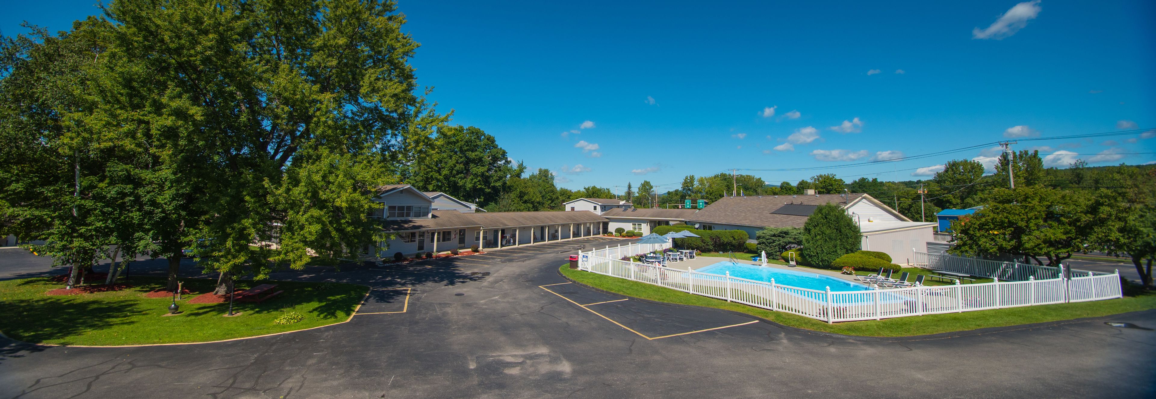 A motel with a swimming pool, a covered parking lot, and a row of single-story buildings.