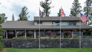 A building with a stone facade, multiple flags, and flower boxes. - Tunnel Mountain Resort (Banff)
