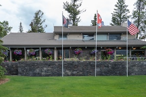 A building with a stone facade, multiple flags, and flower boxes. - Tunnel Mountain Resort (Banff)