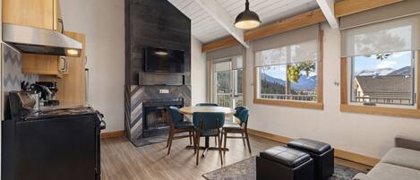 A modern kitchen with a built-in oven, a dining area with a round table and chairs, and a large window offering a mountain view.