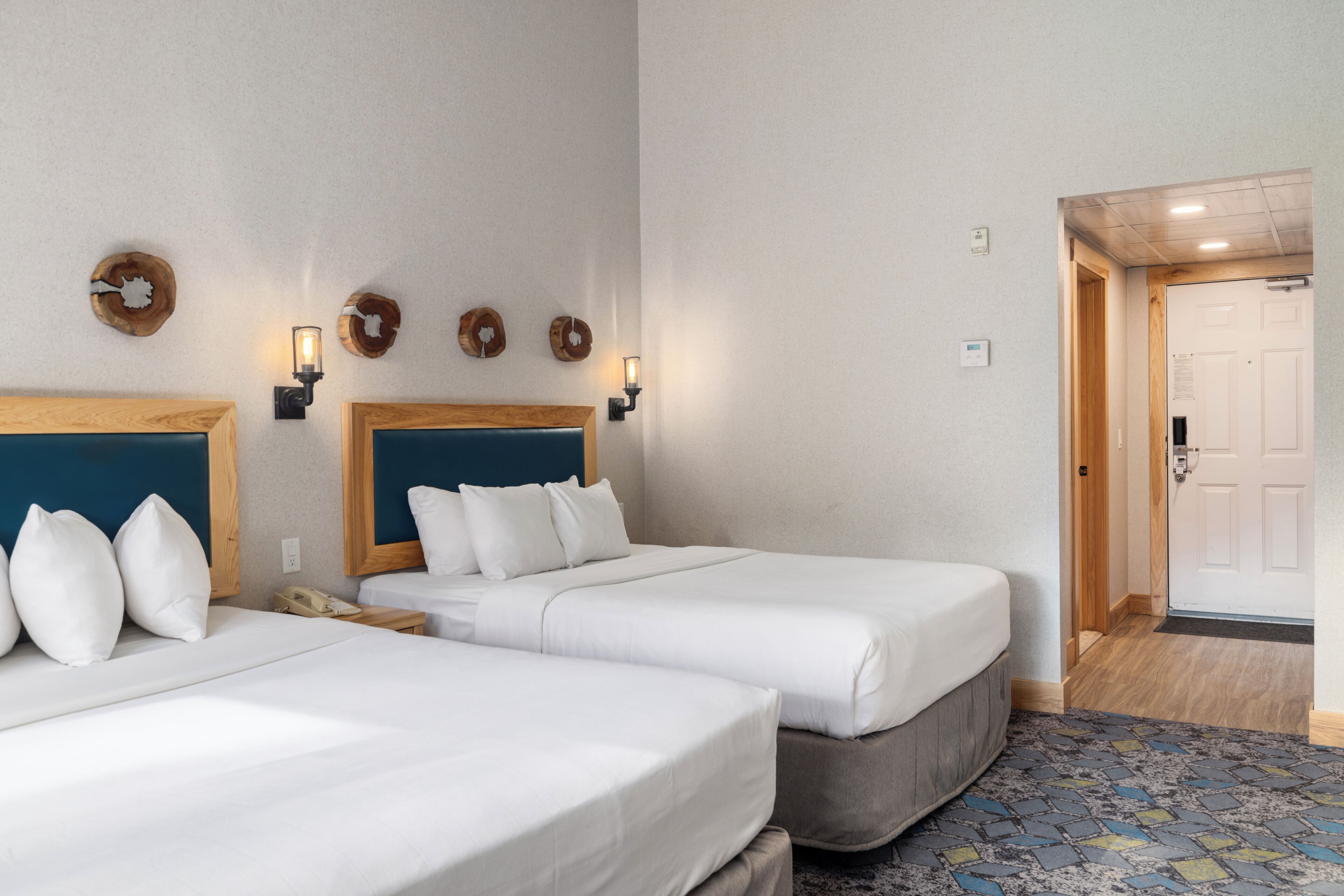 Ein Hotelzimmer mit zwei Betten, einem Holzkopfstück, Wandleuchten und einer Tür zu einem weiteren Raum.