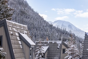 Un chalet de montagne avec un toit en pente et une petite fenêtre, entouré d’arbres couverts de neige et avec une montagne en arrière-plan.