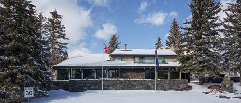 Un edificio cubierto de nieve con fachada de piedra, un asta con una bandera roja y un cartel que indica un límite de velocidad máximo de 30.