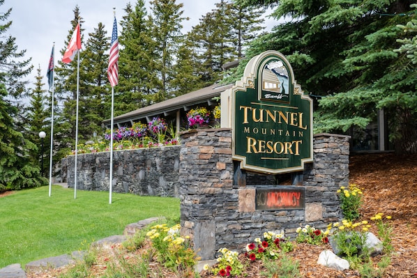 Un panneau indiquant l’emplacement du complexe Tunnel Mountain Resort, avec un mur en pierre et des parterres de fleurs.