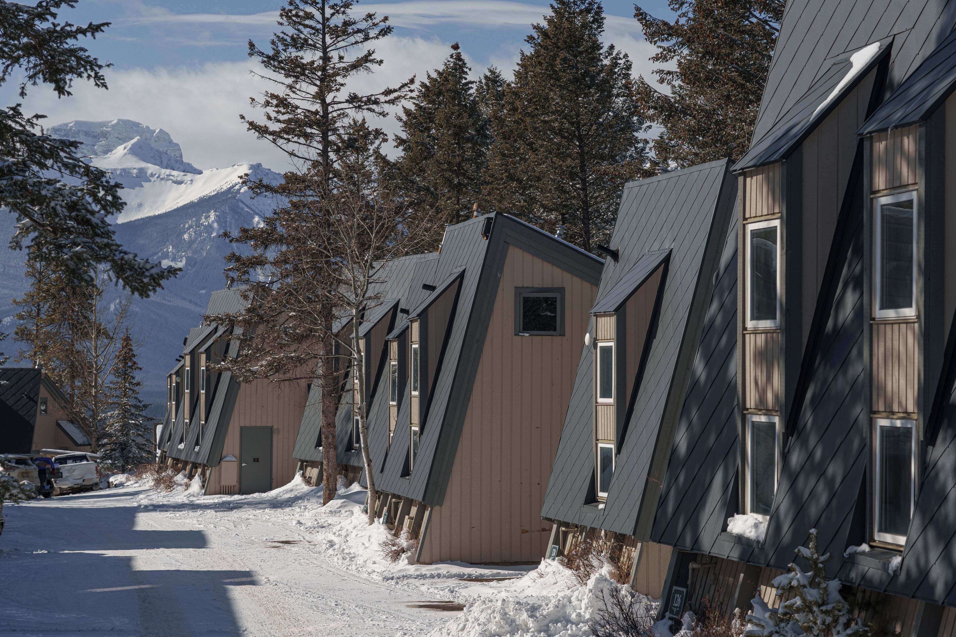 En række chalet-lignende bygninger med skrå tage, placeret på en sneklædt vej med et bjerg i baggrunden.