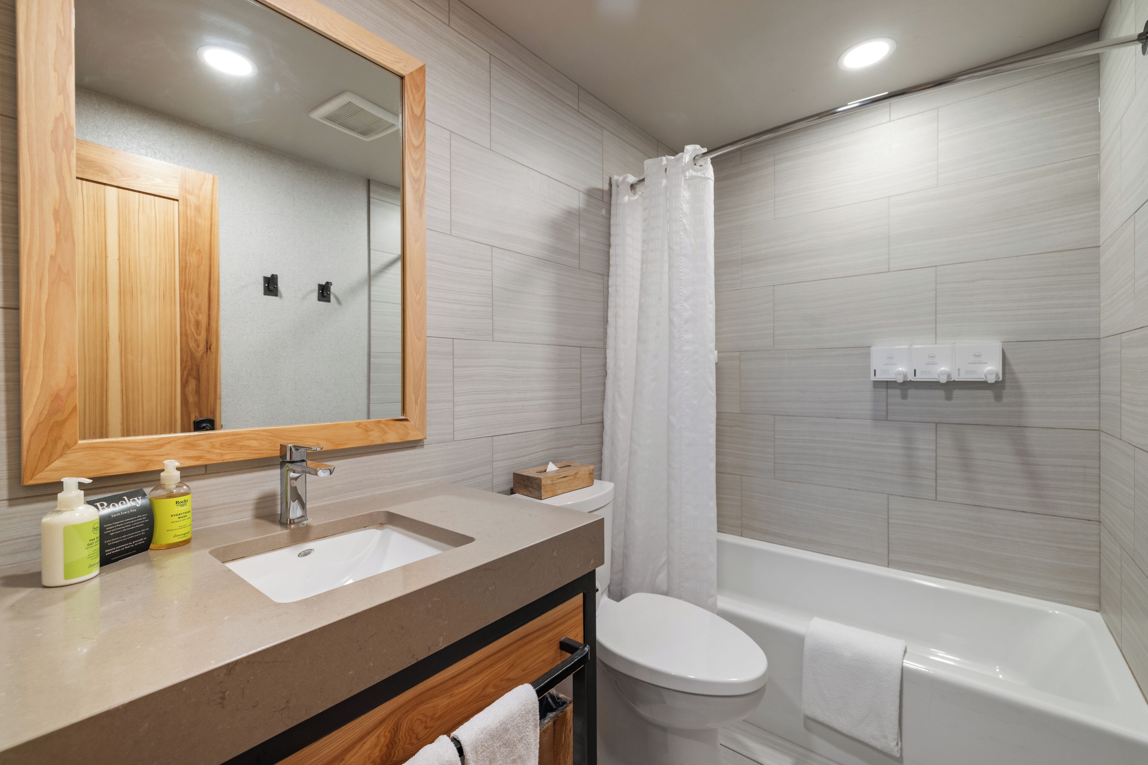 Un baño moderno con tocador de madera, lavamanos, espejo, inodoro y bañera.