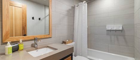 A modern bathroom with a wooden vanity, a sink, a mirror, a toilet, and a bathtub.
