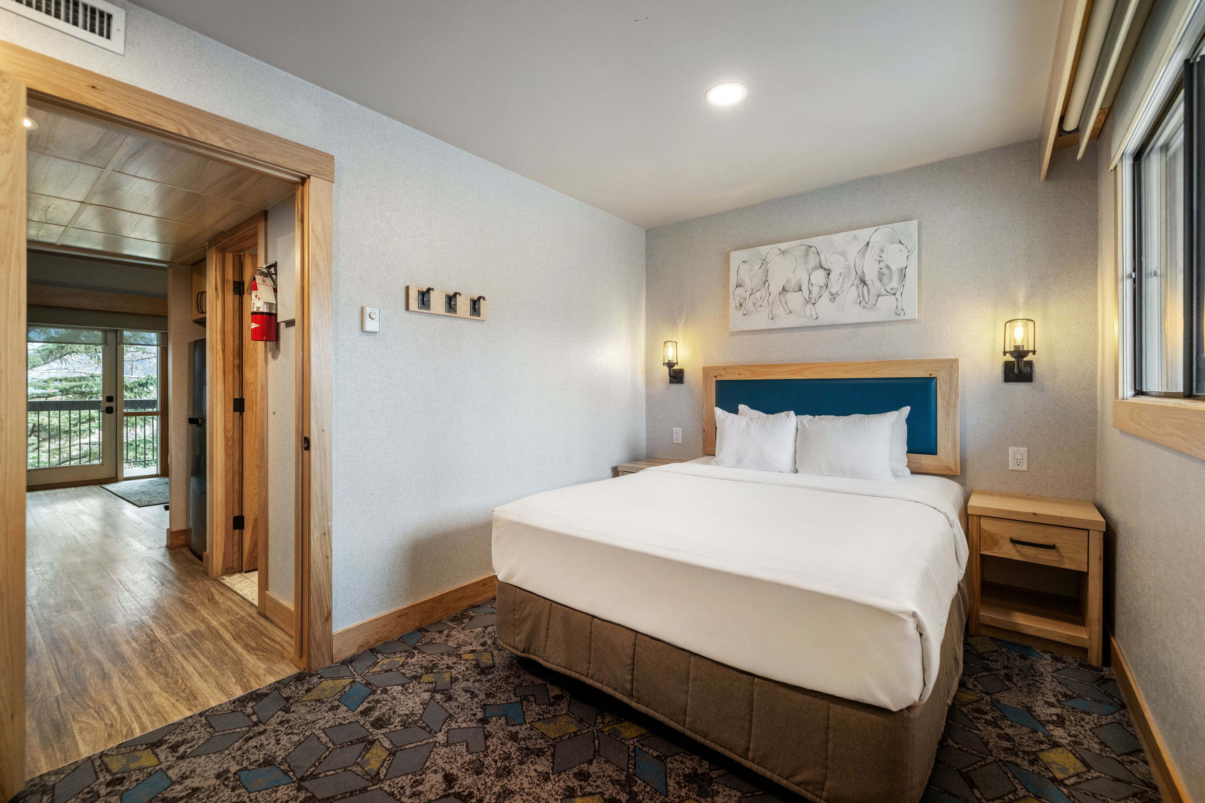 A hotel room with a large bed, a headboard, a nightstand, a wall-mounted light, and a window.