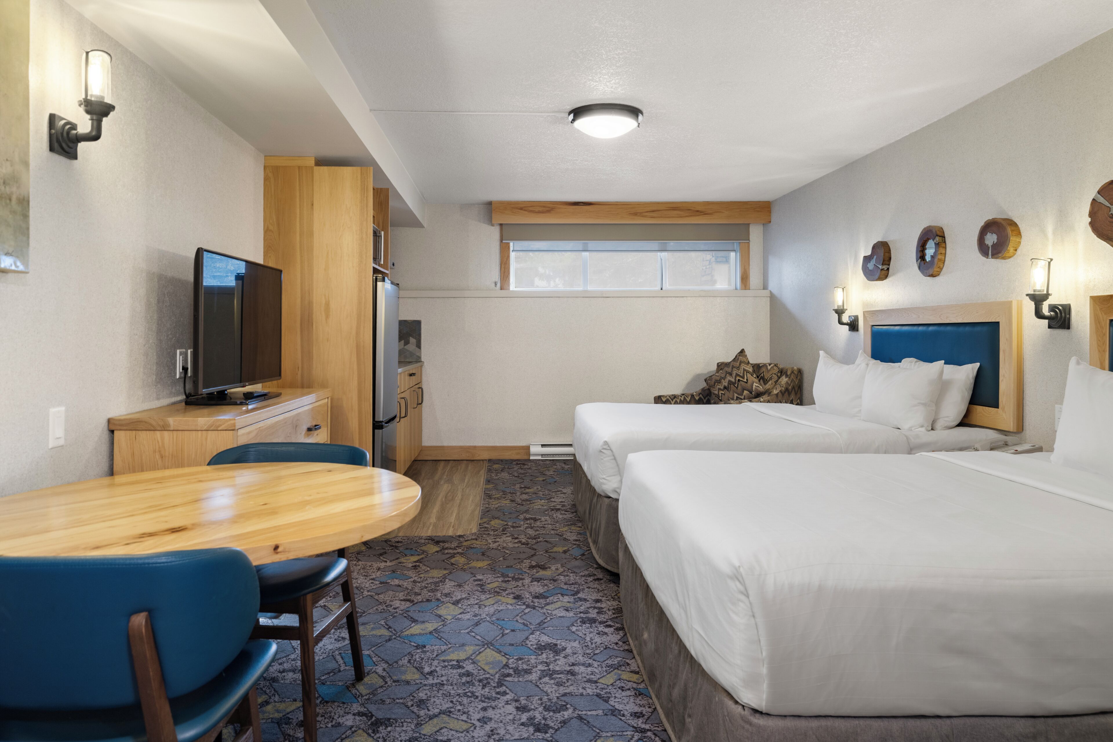 A hotel room with a wooden desk, two beds, a television, and a window.