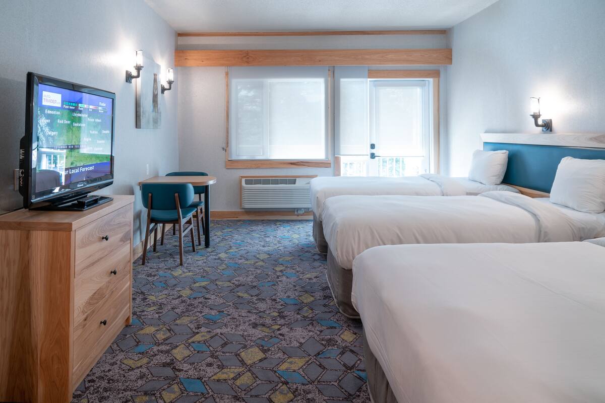 Habitación de hotel con televisor, escritorio, dos camas, alfombra estampada y ventana con vistas.
