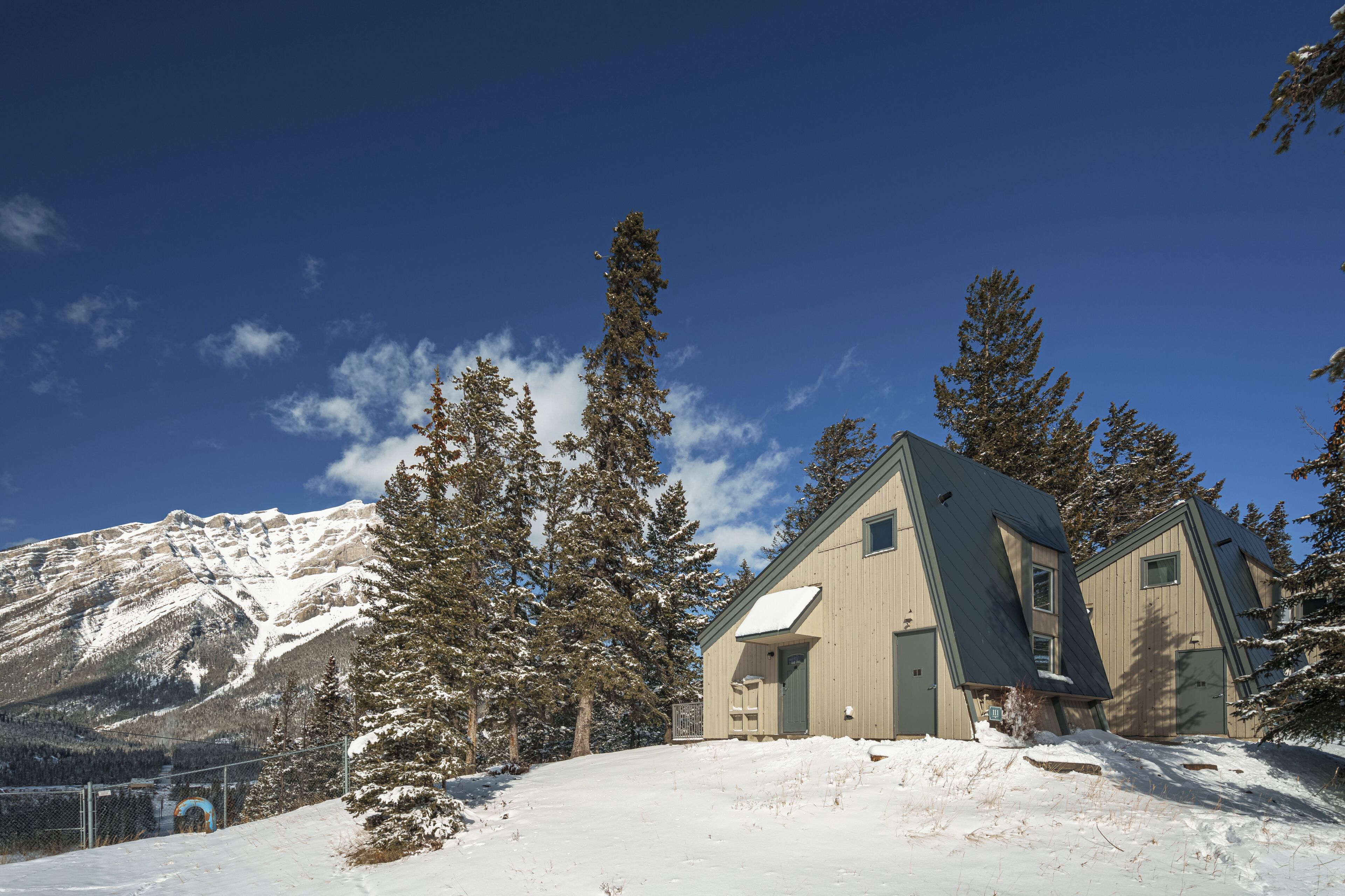 Paesaggio montano innevato con una casetta di legno, un tetto spiovente e un piccolo portico.