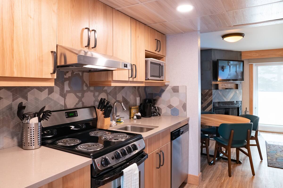 Una cocina moderna con armarios de madera, estufa de acero inoxidable, microondas y un comedor con mesa y sillas.