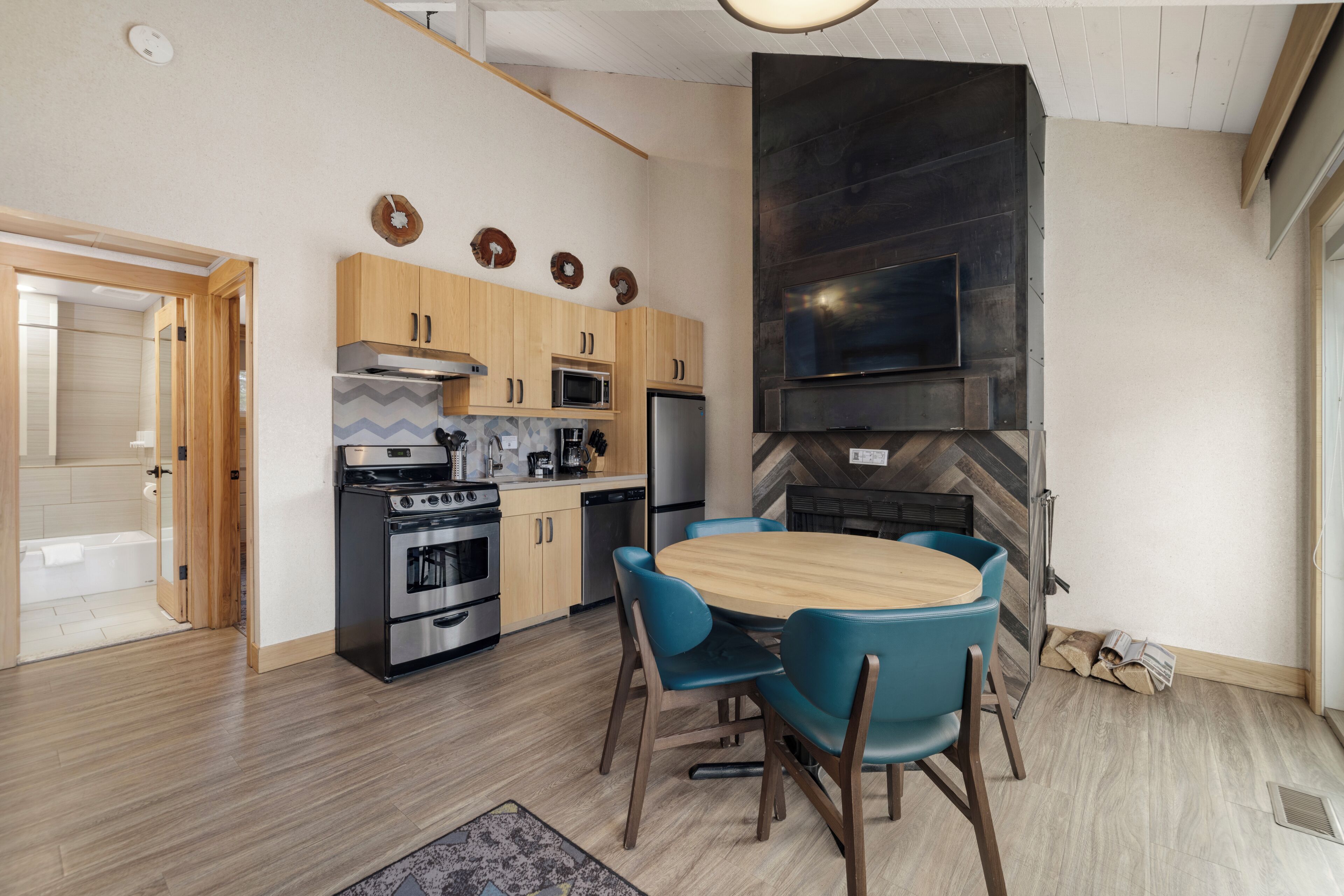 A modern kitchen with wooden cabinets, a built-in oven, microwave, and a large black TV mounted on the wall.