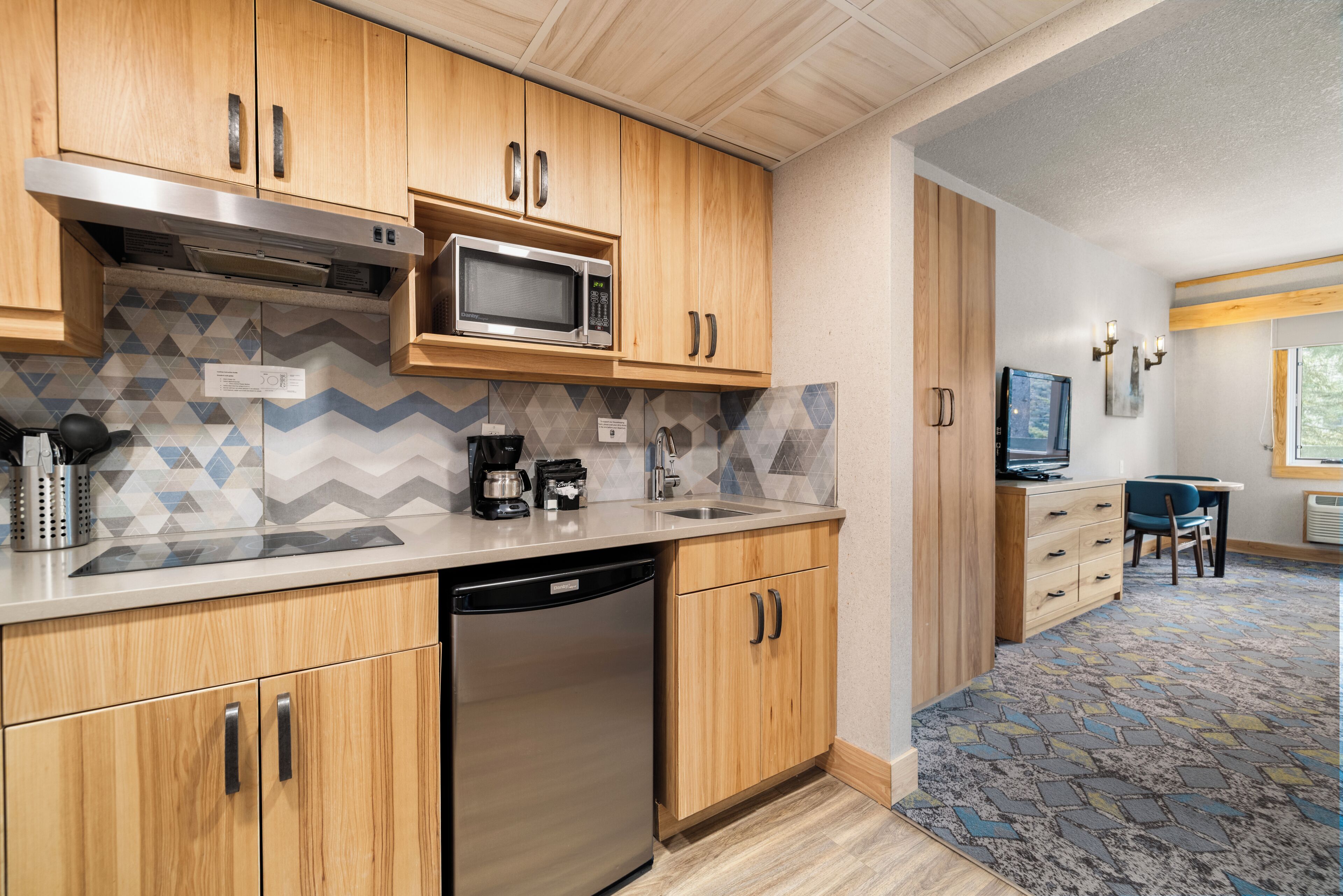 A modern kitchen with wooden cabinets, a built-in microwave, a coffee maker, and a dishwasher.