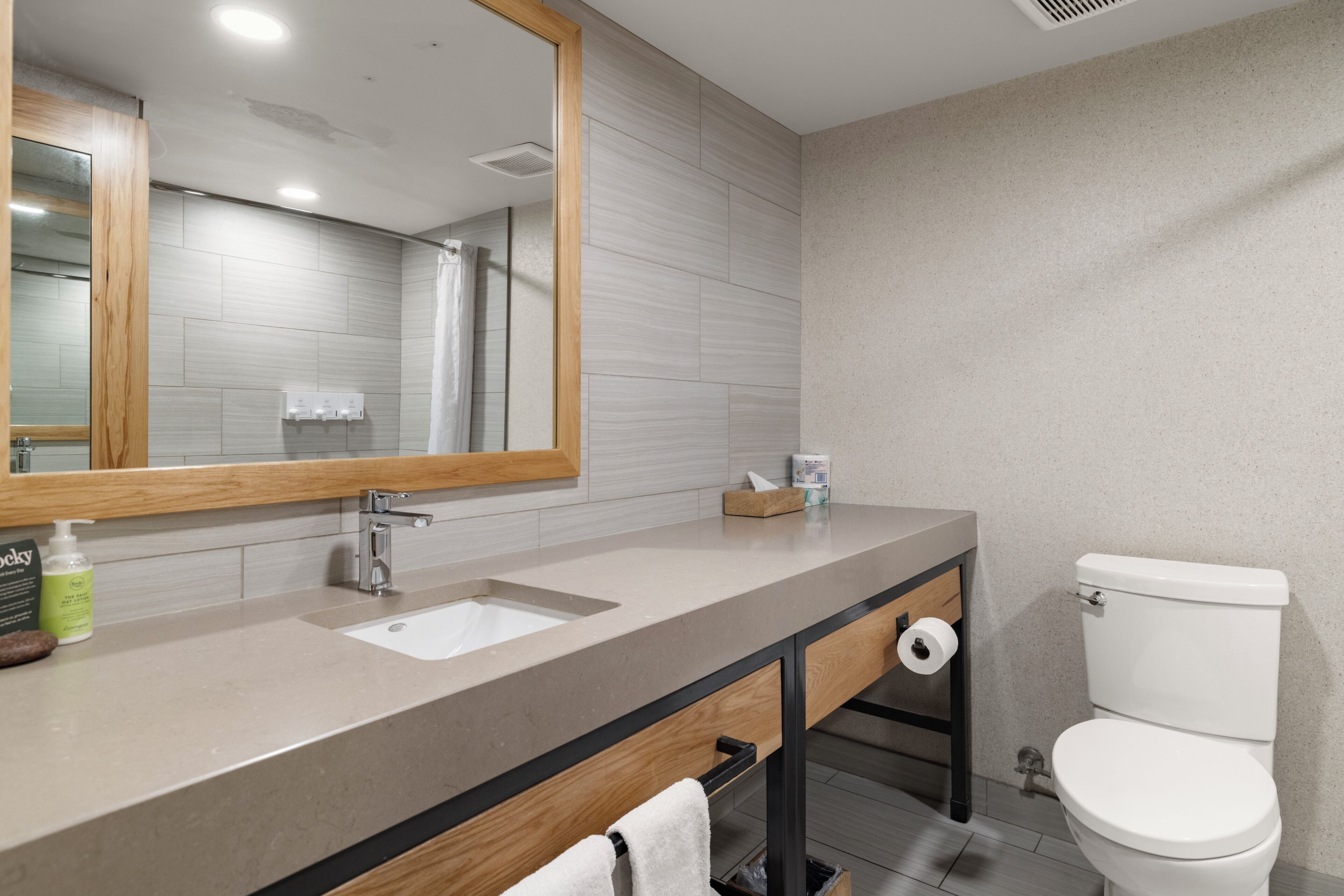 A modern bathroom with a large mirror, a sink, a toilet, and a towel rack.