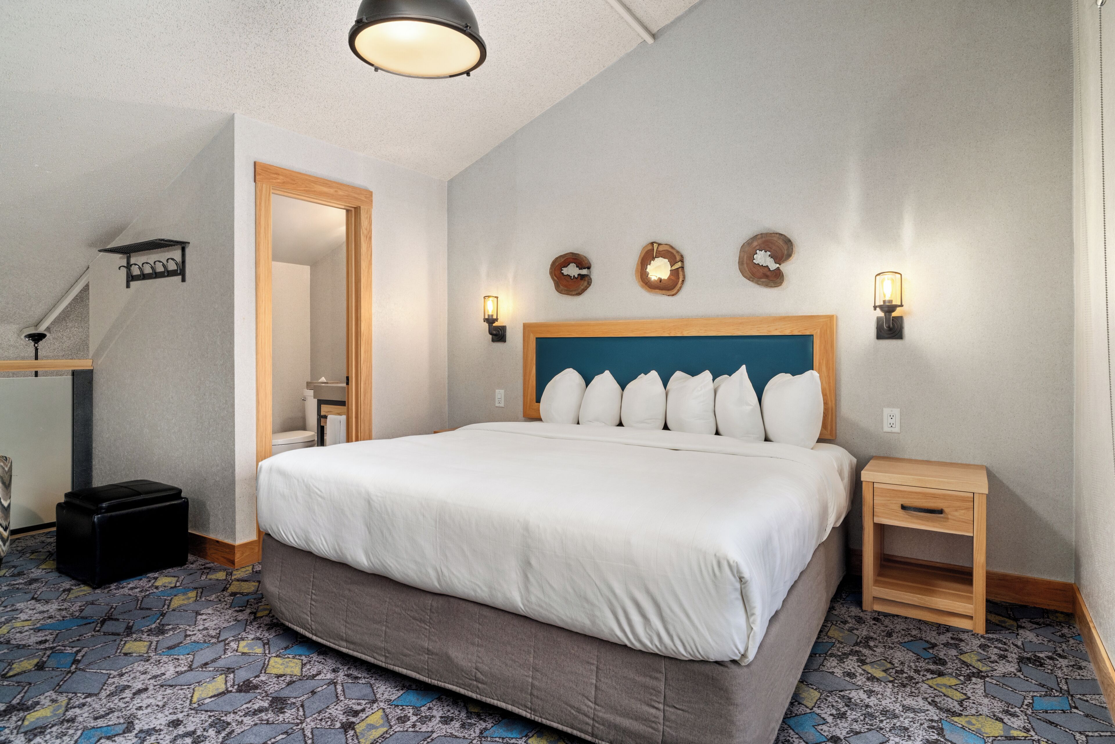 Una habitación de hotel con una cama grande, una mesita de noche, un espejo y una lámpara en el techo.