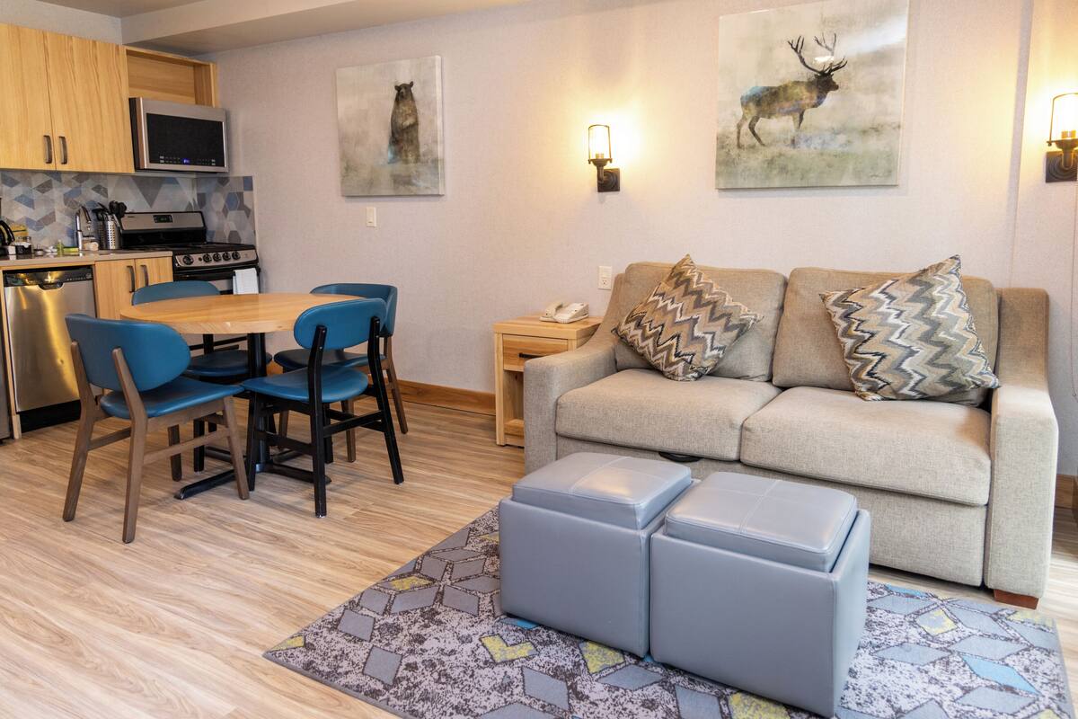 Una sala de estar moderna con un sofá, otomanas y una zona de comedor con sillas y una mesa.