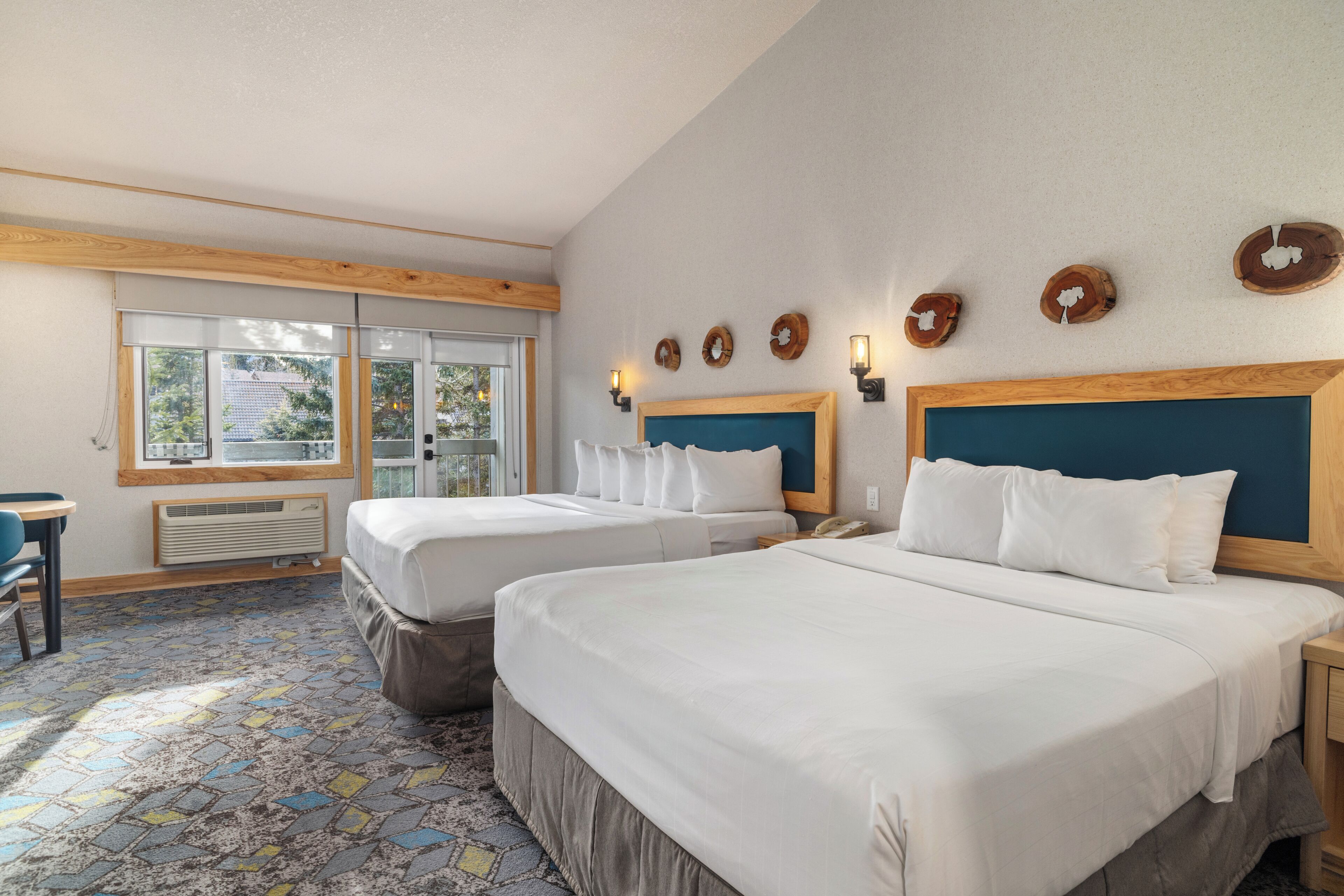 A hotel room with two beds, a window with a view, a desk, and a patterned carpet.