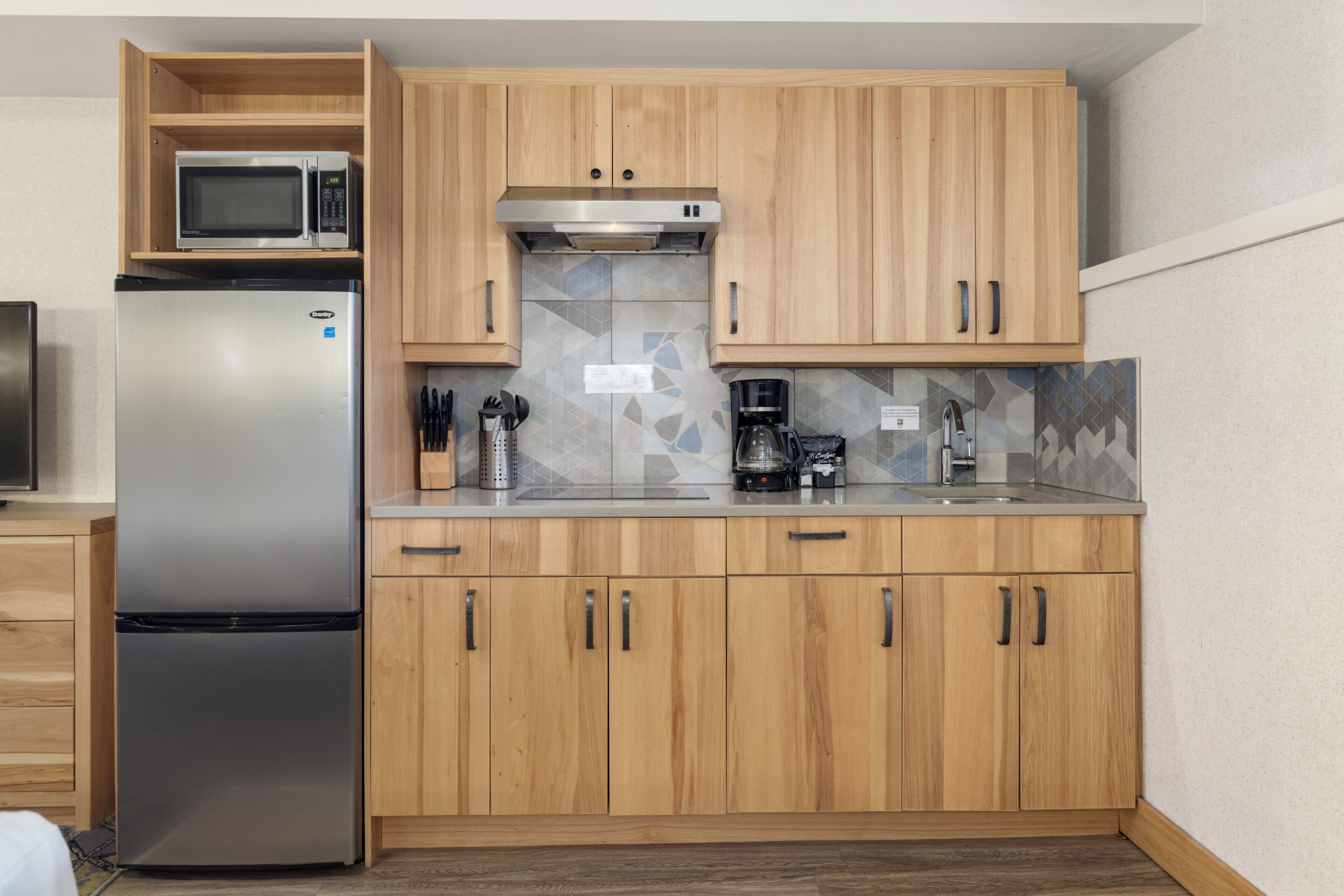 Una cocina moderna con armarios de madera, un refrigerador de acero inoxidable, un microondas, una cafetera y un lavamanos.